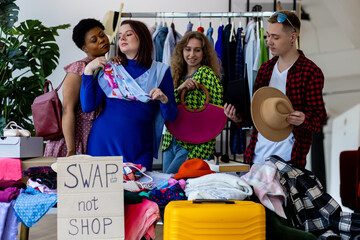 Group of friends generation z girls and boy enjoying home swap party, trying hats, jackets, choosing and exchanging vintage brand clothes, exchange between college young people. Bargain hunting