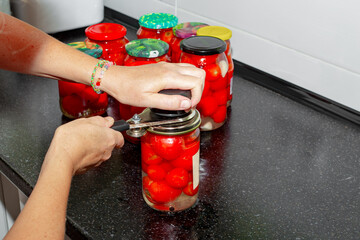 A woman tightens the lids on a jar of red pickled tomatoes with a seamer. Preservation of vegetables.