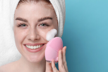 Young woman washing face with brush and cleansing foam on light blue background, closeup. Space for...