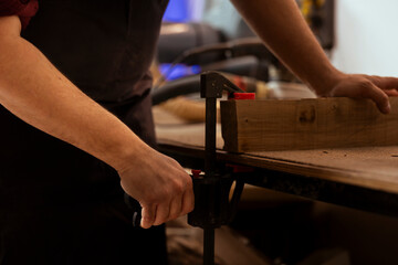 Woodworker using bench vise to hold lumber block, starting furniture assembling in workshop, close...