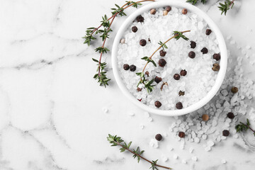 Salt with thyme and peppercorns in bowl on white marble table, flat lay. Space for text
