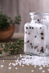 Salt with peppercorns in glass jar and thyme on wooden table