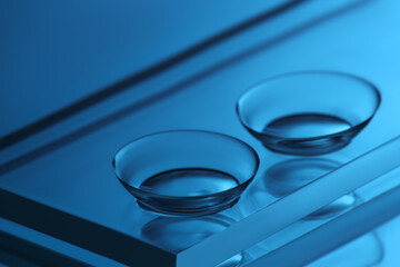 Pair of contact lenses and glass on mirror surface, closeup. Toned in blue