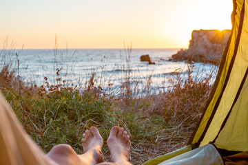watching the sunrise from a tourist tent on the seashore. A woman's legs peek out from a tent