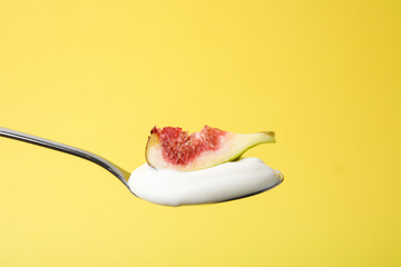 Spoon with yogurt and fig on yellow background, closeup