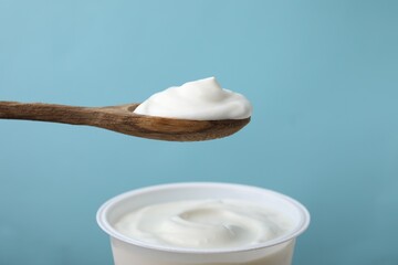 Eating delicious natural yogurt on light blue background