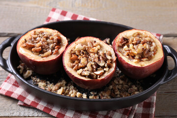 Tasty baked apples with nuts and honey in baking dish on wooden table, closeup