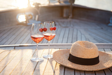 Wine on a yacht in sea. Romantic picnic in summer travel at sunset. Two wineglasses with cherry,...