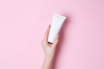 Woman holding tube of cream on pink background, closeup