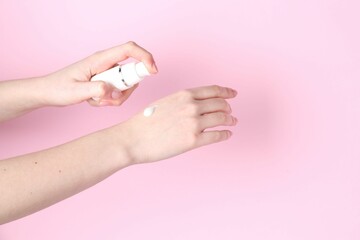 Woman applying cream on her hand against pink background, closeup. Space for text