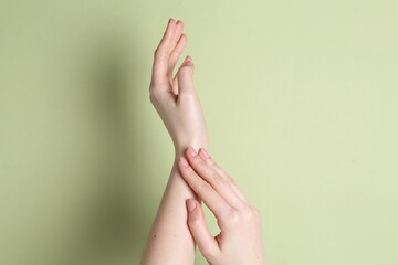 Woman applying cream on her hand against green background, closeup