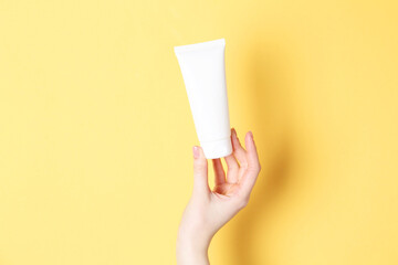 Woman holding tube of cream on yellow background, closeup