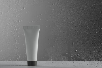 Tube with moisturizing cream on grey background, view through wet glass. Space for text