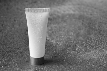 Moisturizing cream in tube on dark wet background, closeup. Space for text