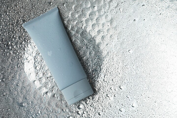 Moisturizing cream in tube on silver background with water drops, top view. Space for text