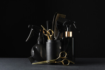 Different hairdresser tools on grey table against black background
