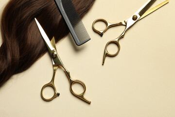 Professional scissors and comb with brown hair strand on beige background, flat lay. Space for text