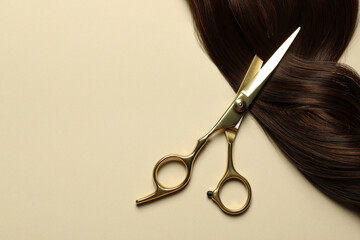 Professional scissors with brown hair strand on beige background, top view. Space for text