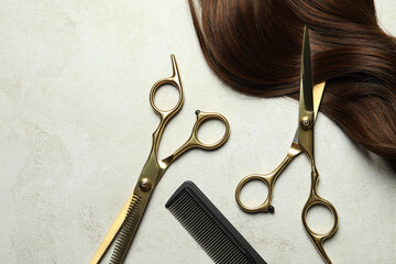 Professional hairdresser scissors and comb with brown hair strand on grey table, flat lay