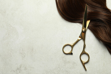 Professional hairdresser scissors with brown hair strand on grey table, top view. Space for text