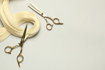 Professional hairdresser scissors with blonde hair strand on light grey background, flat lay. Space...