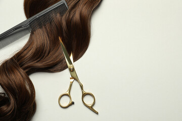 Professional hairdresser scissors and comb with brown hair strand on light grey background, flat...