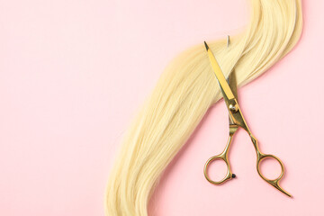Professional hairdresser scissors with blonde hair strand on pink background, top view. Space for...