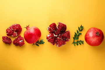 Fresh pomegranates and green leaves on yellow background, flat lay