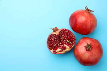 Whole and cut fresh pomegranates on light blue background, flat lay. Space for text