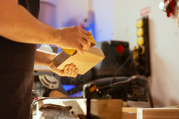 Man in studio using sandpaper for sanding wooden surface before painting it, ensuring adequate...