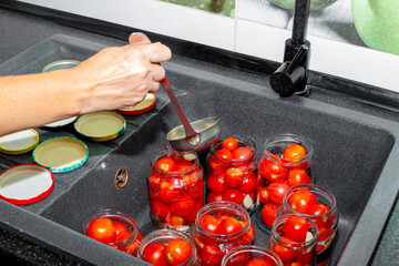 Canning tomatoes. A woman pours brine into jars with red ripe tomatoes