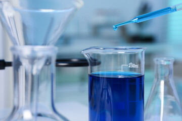 Laboratory analysis. Dripping blue liquid into beaker on table, closeup