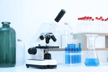 Laboratory analysis. Different glassware with blue liquid and microscope on white table indoors