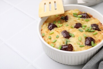 Tasty sausage casserole with green onions in baking dish served on white tiled table, closeup