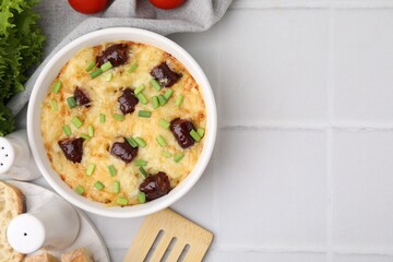 Tasty sausage casserole with green onions in baking dish served on white tiled table, flat lay....