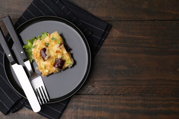 Tasty sausage casserole with green onions and cutlery served on wooden table, top view. Space for text