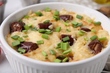 Tasty sausage casserole with green onion in baking dish on white table, closeup