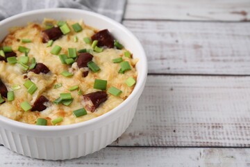 Tasty sausage casserole with green onion in baking dish on white wooden table, closeup. Space for text