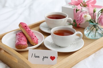 Tasty breakfast served in bed. Delicious eclairs, tea, gift box, flowers and card with phrase I Love You on tray