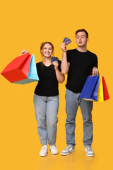 Obraz premium Young couple with credit cards and shopping bags on yellow background