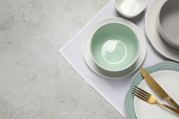 Beautiful ceramic dishware and cutlery on light grey table, top view. Space for text