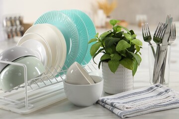 Many different clean dishware, cutlery and houseplant on white marble table in kitchen