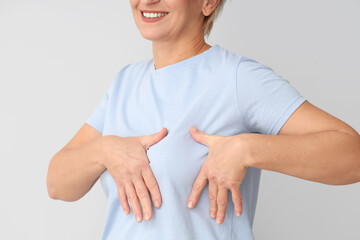 Mature woman checking her breast on light background, closeup. Cancer awareness concept