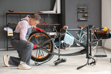 Mature mechanic repairing bicycle wheel in workshop