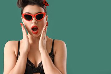 Shocked young pin-up woman in sunglasses on green background, closeup