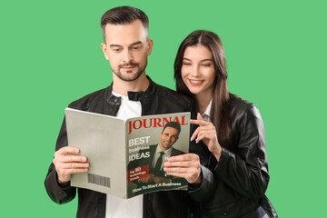 Cool young couple reading magazine on green background