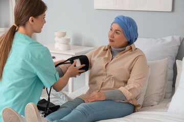 Mature woman after chemotherapy with nurse measuring blood pressure in bedroom. Stomach cancer...