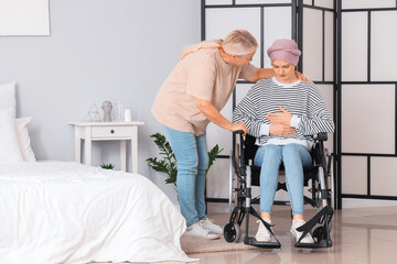 Young woman after chemotherapy in wheelchair with her mother at home. Stomach cancer concept