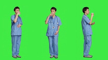 Healthcare specialist enjoying hot coffee cup against greenscreen backdrop, drinking caffeine refreshment in blue scrubs. Medical assistant serving beverage at work, friendly staff. Camera A.