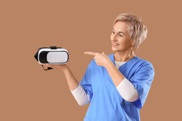 Mature female dentist pointing at VR glasses on brown background